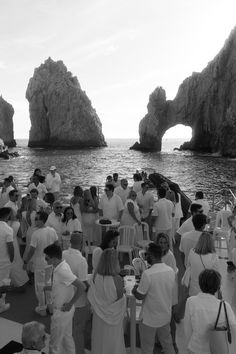 a group of people standing on top of a boat near the ocean and rock formations