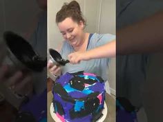 a woman is holding a spoon over a cake with blue and pink designs on it