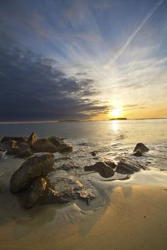 the sun is setting over some rocks on the beach