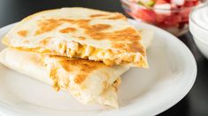 two quesadillas sitting on a white plate next to a bowl of salad