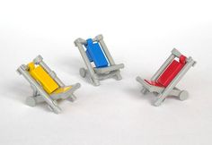 three miniature chairs sitting next to each other on a white surface with one red, one blue and one yellow