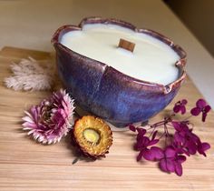 a candle and some purple flowers on a wooden table next to a flower pot filled with milk