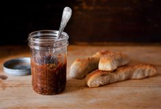 a jar filled with food sitting on top of a wooden cutting board next to bread