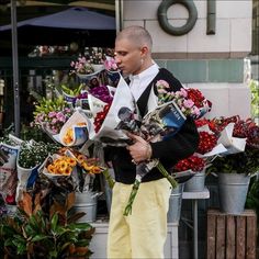 a man standing in front of a bunch of flowers holding onto some papers and looking at something