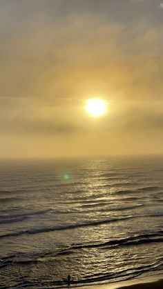 the sun is setting over the ocean with people walking on the beach in the foreground