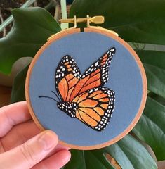 a hand holding up a small embroidery project with a butterfly on it's back