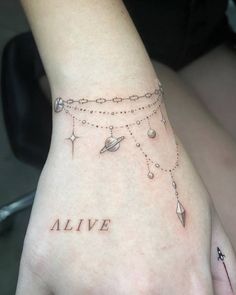 a woman's hand with a tattoo on it that says alive and planets hanging from the wrist