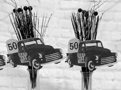 two vases filled with sticks and flowers in front of a brick wall, each holding an old car