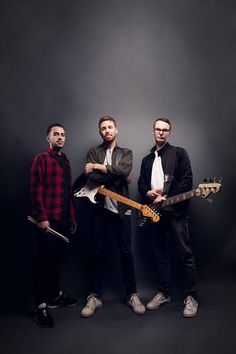 three men standing next to each other with guitars in their hands and looking at the camera