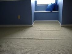 an empty room with blue walls and a window seat on the far wall is a carpeted floor