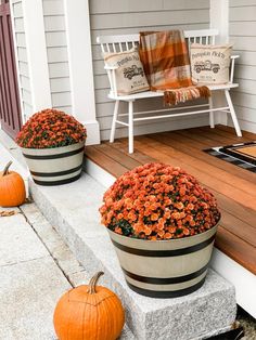 two pumpkins are sitting on the front porch next to some planters with flowers in them