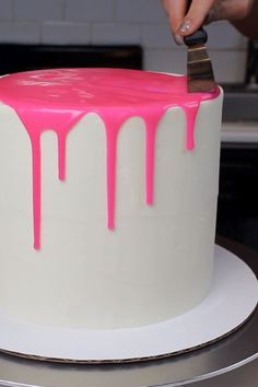 a person is cutting into a cake with pink icing on the top and bottom