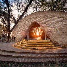 an outdoor stage with steps leading up to it and the sun shining through the trees