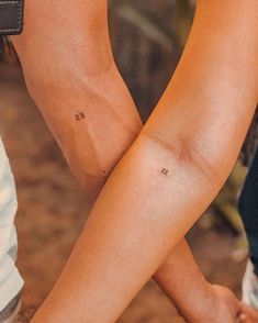 two people with small tattoos on their arms and legs, one is holding the other's hand