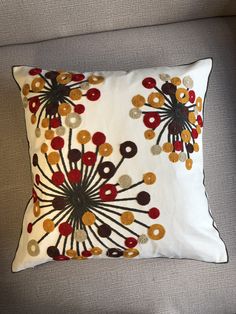 a white pillow with red, yellow and brown flowers on it sitting on a couch