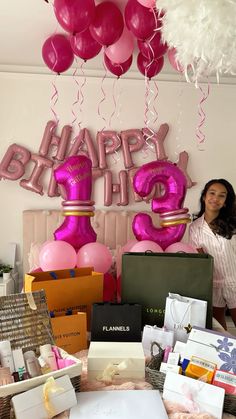 a woman standing in front of a table filled with pink and white balloons that spell happy birthday