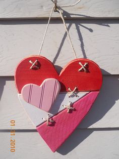 two wooden hearts hanging from a string on a white wall with cross pins attached to them