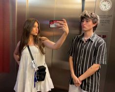 two young people standing in front of an elevator taking pictures with their cell phones and cameras