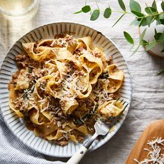 a white plate topped with pasta covered in meat and cheese next to a glass of wine