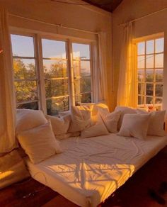 a bed with lots of pillows on top of it in front of two large windows