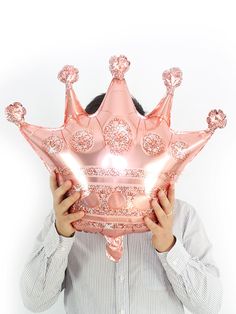 a woman holding up a pink crown shaped pillow in front of her face with both hands