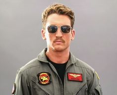 a man wearing sunglasses and an air force pilot's uniform is standing in front of a gray background