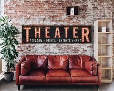 a couch in front of a brick wall with the word theater on it and a potted plant next to it