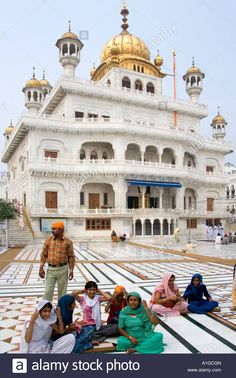 people sitting on the ground in front of a white building with gold domes, india - stock image