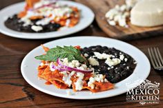 two white plates topped with black beans, cheese and green leafy garnish