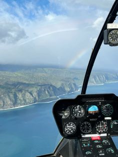 the view from inside an airplane looking out at the ocean and mountains with a rainbow in the sky