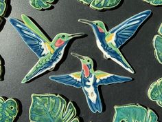 three ceramic hummingbirds sitting on top of green leaves