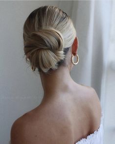 a woman with blonde hair in a low bun wearing gold hoop earrings, looking out the window