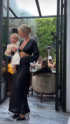 a woman standing next to a child in front of a glass door with people sitting around