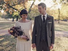 a man and woman standing next to each other in a field with trees behind them