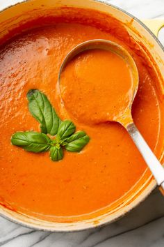 a bowl of tomato soup with basil on top and a spoon in the bowl next to it