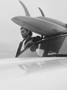 a man holding two surfboards on top of his head while sitting in a car