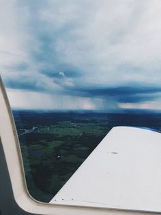 the view from inside an airplane looking out at green fields and blue sky with white clouds