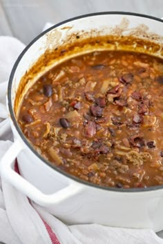 a white pot filled with chili and beans on top of a table next to a napkin