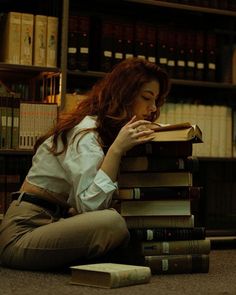 a woman sitting on the floor next to a stack of books in front of a bookcase