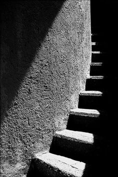 black and white photograph of steps leading up to the sky in an alleyway with shadows on the wall