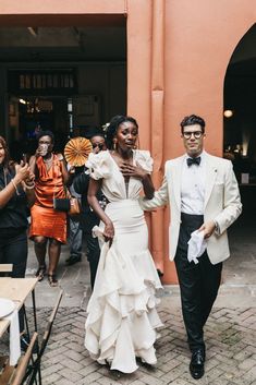 a man and woman in formal wear walking down the street with other people behind them