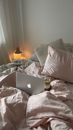 an apple laptop computer sitting on top of a bed covered in pink sheets and pillows