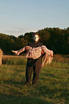 a man in a costume carrying a dead person on his back through a field with hay bales