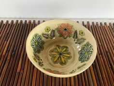 a bowl with flowers painted on it sitting on top of a bamboo mat in front of a white wall