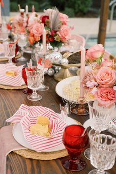 the table is set with pink flowers, plates and silverware for dinner guests to eat