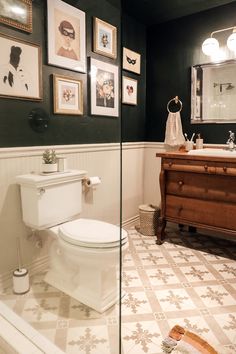 a white toilet sitting in a bathroom next to a wooden dresser and mirror with pictures on the wall