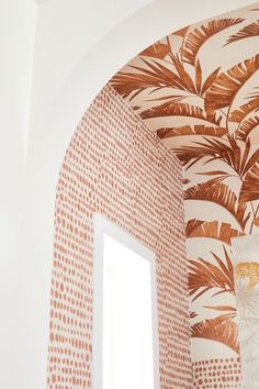 an arched window in the corner of a room with wallpaper and palm leaves on it