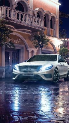 a white car parked in front of a building on a wet street at night with its lights on