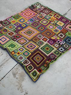 a multicolored blanket is laying on the ground with it's edges crocheted