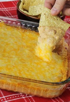 a person dipping a tortilla chip into a casserole dish with cheese